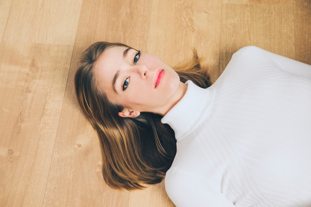 Thoughtful woman lying on wooden floor