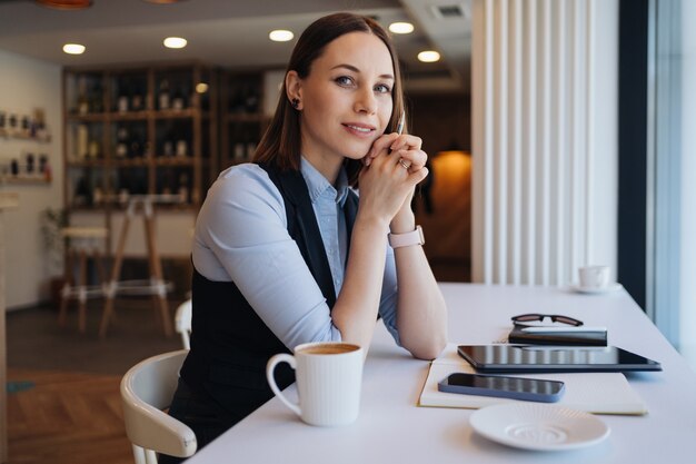 コーヒーマグとカフェテリアに座っている思いやりのある女性。考えながらお茶を飲む中年女性。コーヒーを飲みながらリラックスして考えます。