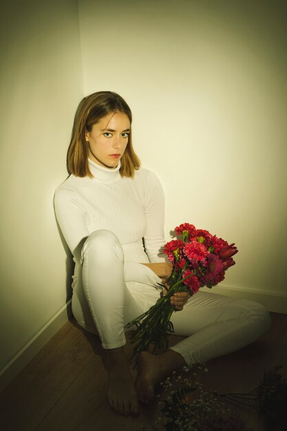 花の花束を床に座っている思いやりのある女性