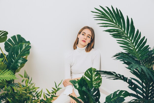Thoughtful woman sitting on floor with green plants