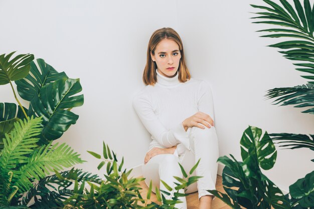 Thoughtful woman sitting on floor with plants