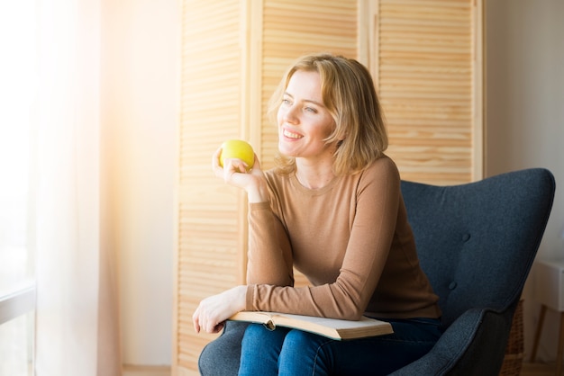 Бесплатное фото Вдумчивый женщина, сидящая с книгой и яблоком