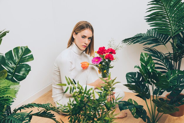 緑の植物の近くの花と座っている思いやりのある女性