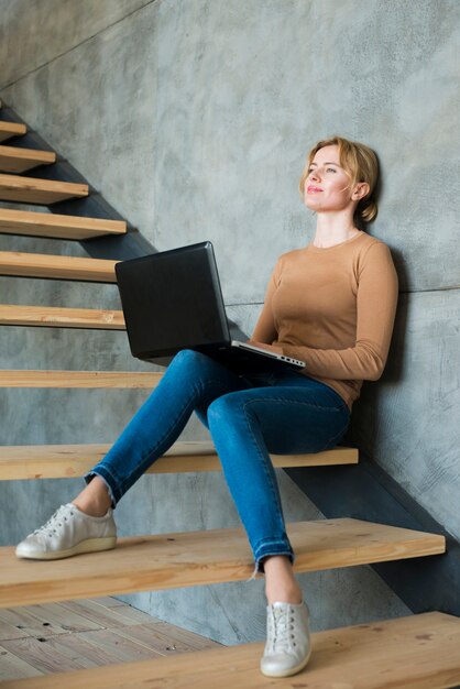 Вдумчивый женщина, используя ноутбук на лестнице
