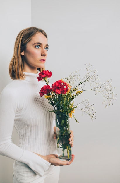 Thoughtful woman with bright flowers in vase at wall