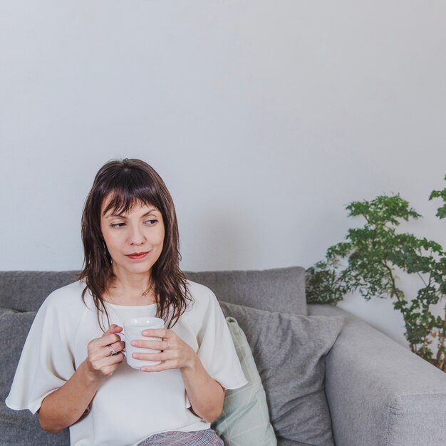 ソファにコーヒーを持つ思いやりのある女性