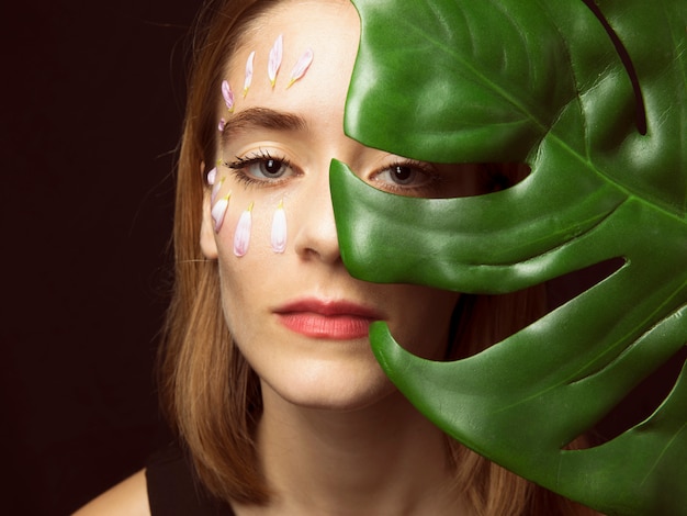 Вдумчивый женщина с лепестками цветов на лице и зеленых листьев