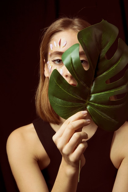 Free photo thoughtful woman with flower petals on face and leaf