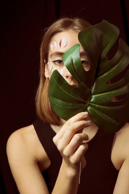 Thoughtful woman with flower petals on face and leaf