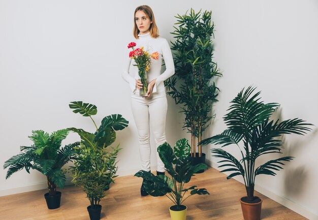 Thoughtful woman with flowers in vase near green plant 