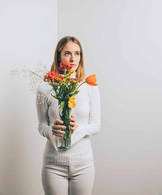 Free photo thoughtful woman with flowers in vase
