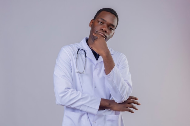 잠겨있는 표정으로 턱에 손으로 청진기와 흰색 코트를 입고 사려 깊은 젊은 아프리카 계 미국인 남성 의사