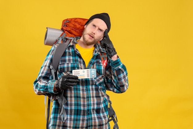 Free photo thoughtful young backpacker with black hat holding plane ticket