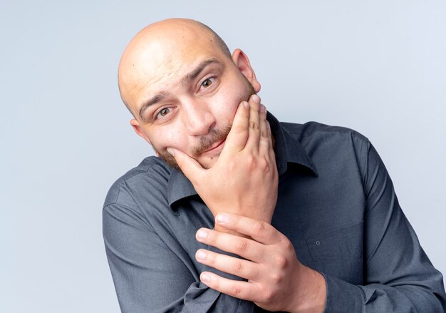 Thoughtful young bald call center man looking at front putting hand on chin and holding wrist isolated on white wall