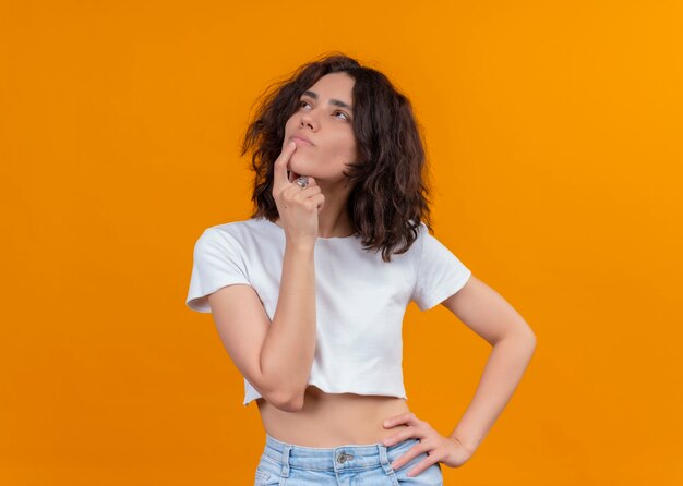 Thoughtful young beautiful woman putting finger on lip on isolated orange wall with copy space