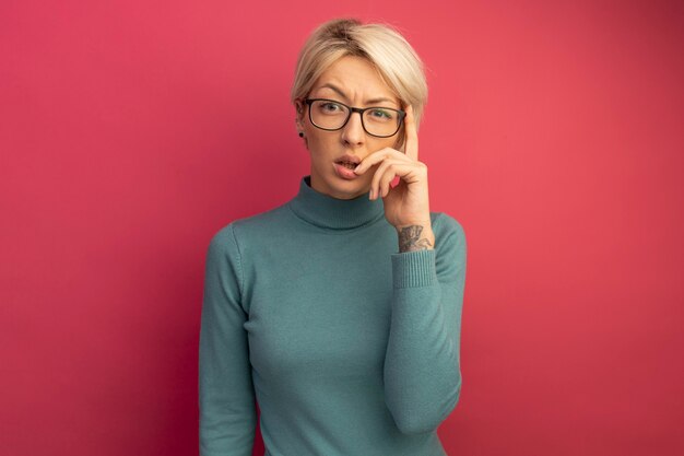 Thoughtful young blonde girl wearing glasses doing think gesture 