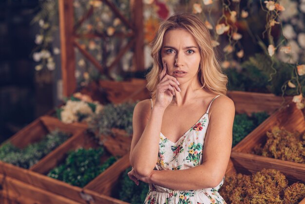 Thoughtful young blonde woman in floral dress standing in front of wooden crate