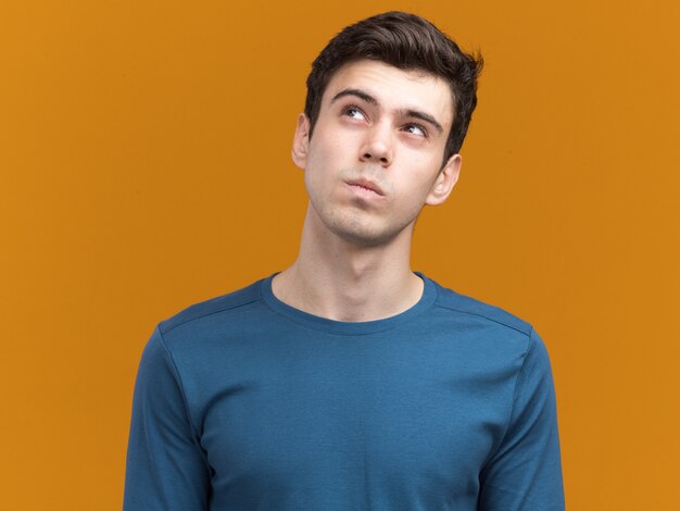 Thoughtful young brunette caucasian boy looking up on orange