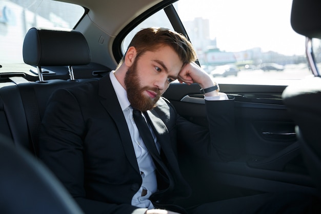 Free photo thoughtful young businessman holding hand on forehead and looking away