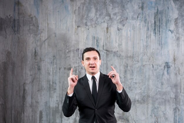 Thoughtful young businessman raising pointing fingers