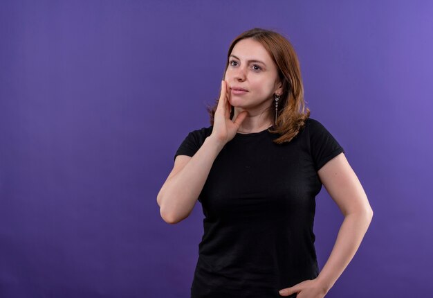 Thoughtful young casual woman putting hand on cheek on isolated purple wall with copy space