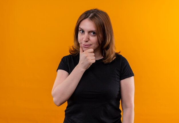 Thoughtful young casual woman putting hand on chin on isolated orange wall with copy space