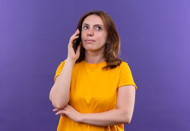 Задумчивая молодая случайная женщина разговаривает по телефону на изолированной фиолетовой стене с копией пространства