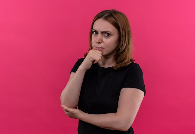 Thoughtful young casual woman with hand on chin on isolated pink wall with copy space