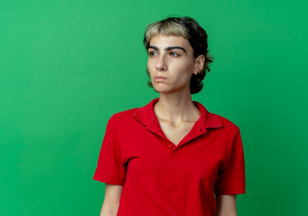 Thoughtful young caucasian girl with pixie haircut looking at side isolated on green background with copy space