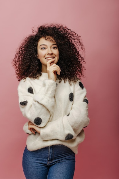 Free photo thoughtful young caucasian lady with curly black hair looks enthusiastically at camera indoors girl model in casual winter clothes leisure lifestyle and beauty concept