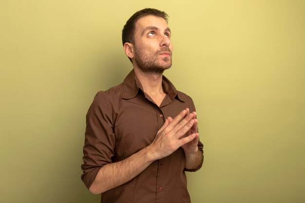 Thoughtful young caucasian man keeping hands together looking up isolated on olive green background with copy space