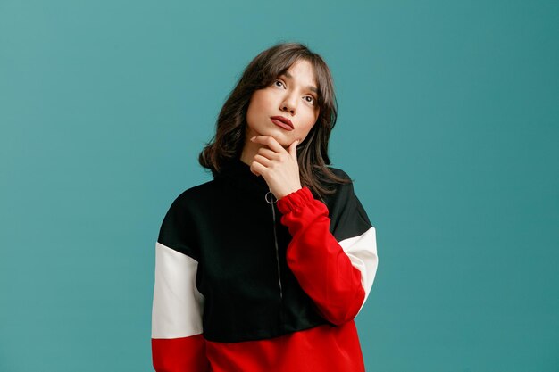 Thoughtful young caucasian woman keeping hand on chin looking up isolated on blue background