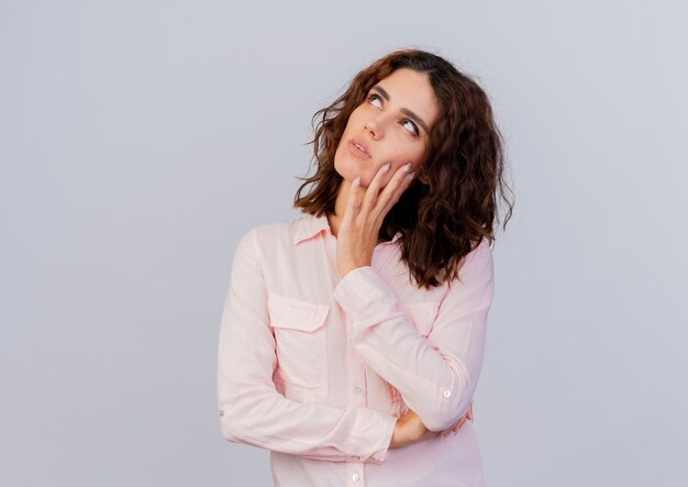 Thoughtful young caucasian woman puts hand on face looking up