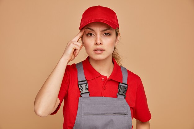 思いやりのある若い女性の建設労働者は、制服とキャップを身に着けている思考ジェスチャーをしています