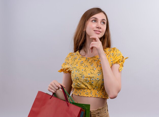 Thoughtful young girl holding paper bags and putting hand on chin on isolated white wall