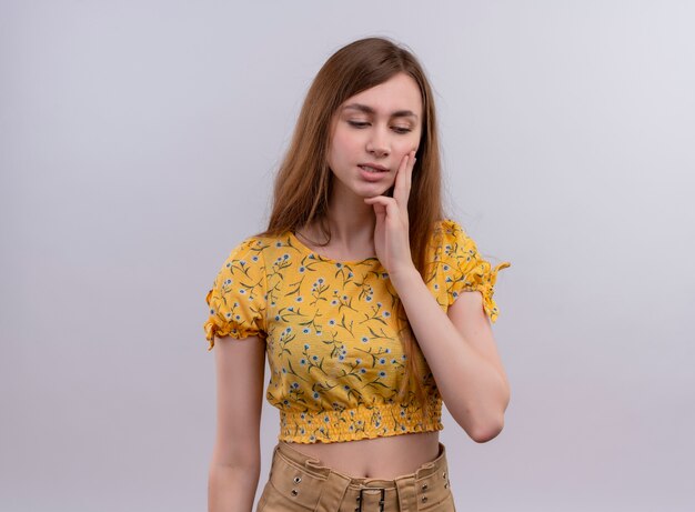 Thoughtful young girl putting hand on cheek and looking down on isolated white wall with copy space