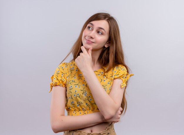 Thoughtful young girl putting hand on chin on isolated white wall with copy space