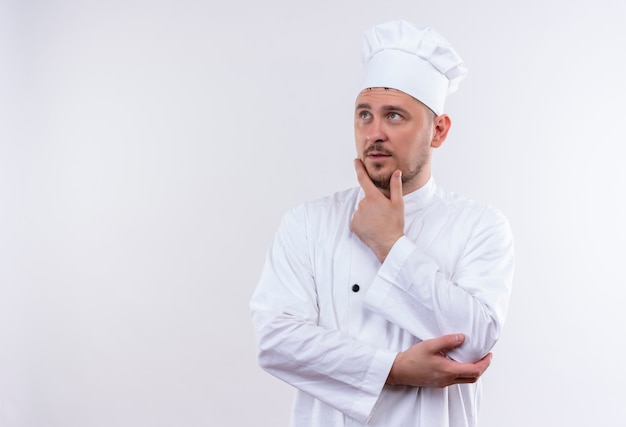 흰색 공간에 고립 된 측면을보고 턱에 손을 넣어 요리사 유니폼 사려 깊은 젊은 잘 생긴 요리사