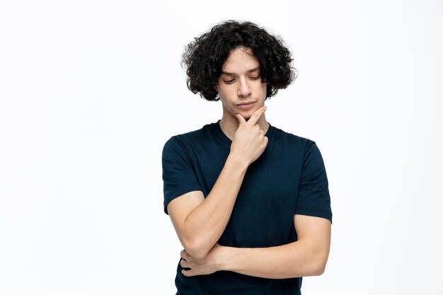 Thoughtful young handsome man keeping hand on chin looking down isolated on white background with copy space