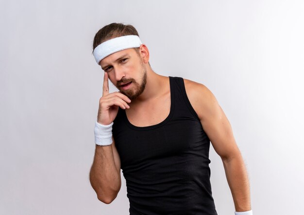 Free photo thoughtful young handsome sporty man wearing headband and wristbands putting finger on face looking  isolated on white space