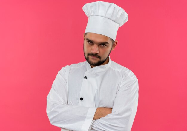 Foto gratuita giovane cuoco maschio premuroso in uniforme del cuoco unico che sta con la postura chiusa che sembra isolata sullo spazio rosa