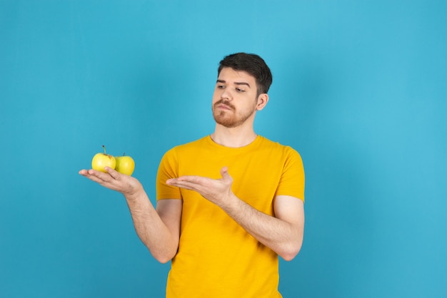 Thoughtful young man holding fresh organic apples and looking at it .