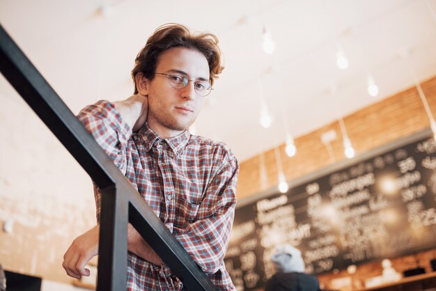 Thoughtful young man is sitting in confectionery shop. She is drinking coffee while waiting for someone