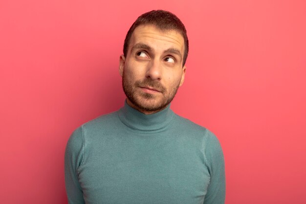 Thoughtful young man looking at side isolated on pink wall