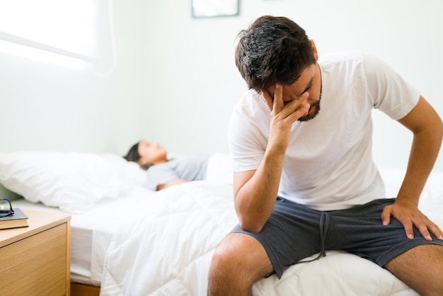 Foto gratuita giovane premuroso in pigiama seduto sul letto al mattino e triste per la sua cattiva relazione