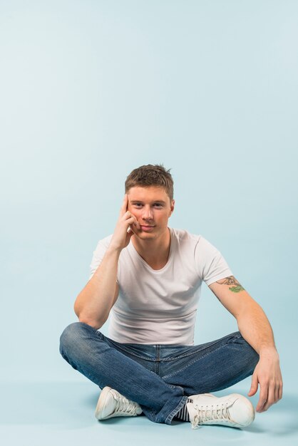 Thoughtful young man sitting on floor with his crossed legs against white background