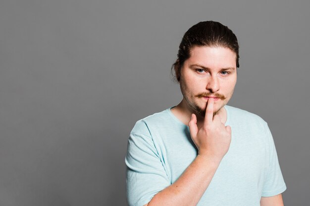 Thoughtful young man with his hand on lips against grey background