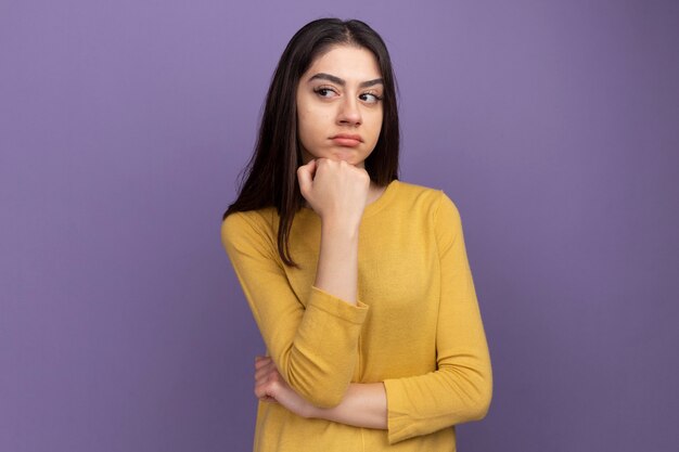 Thoughtful young pretty caucasian girl keeping hand under chin looking at side 