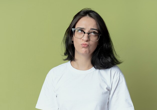 Thoughtful young pretty caucasian girl looking at side wearing glasses isolated on olive green background