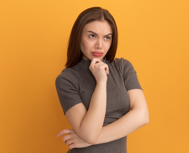 Thoughtful young pretty woman putting hand on chin looking straight 